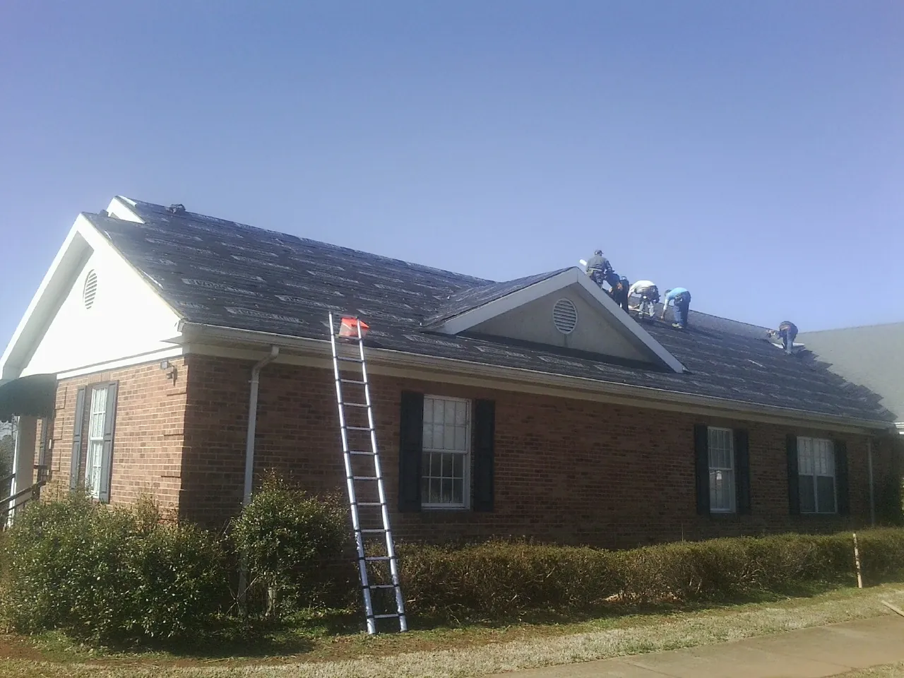 Crew tearing shingles off a brick ranch roof with a ladder set — Emergency Roof Repair work by our crew in Fairdale