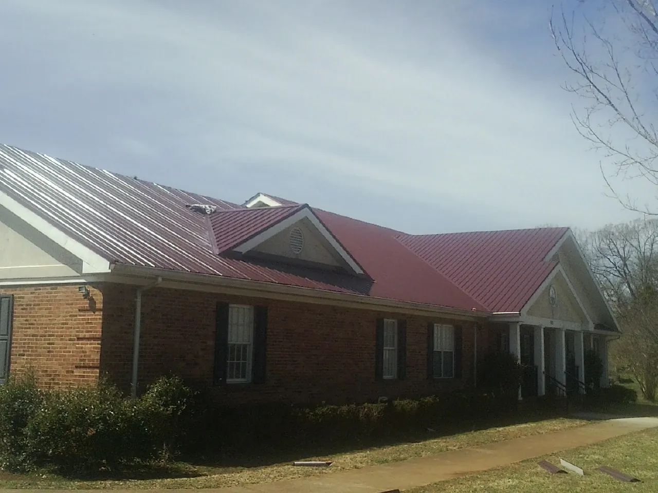 Red metal roof with gabled entries on a long brick building, from a Hail Damage Roof Repair job in Fairdale