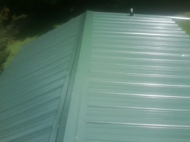 New green metal panels meeting at the ridge of a roof — Flat Roof Repair work by our crew in Fairdale