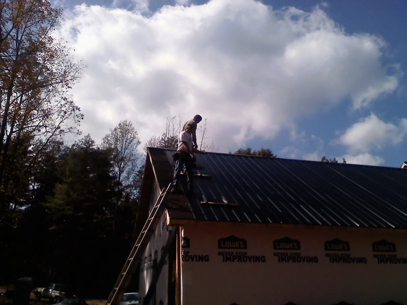 Roofer fastening dark metal panels high against a cloudy sky, from a Roof Inspection job in Fairdale