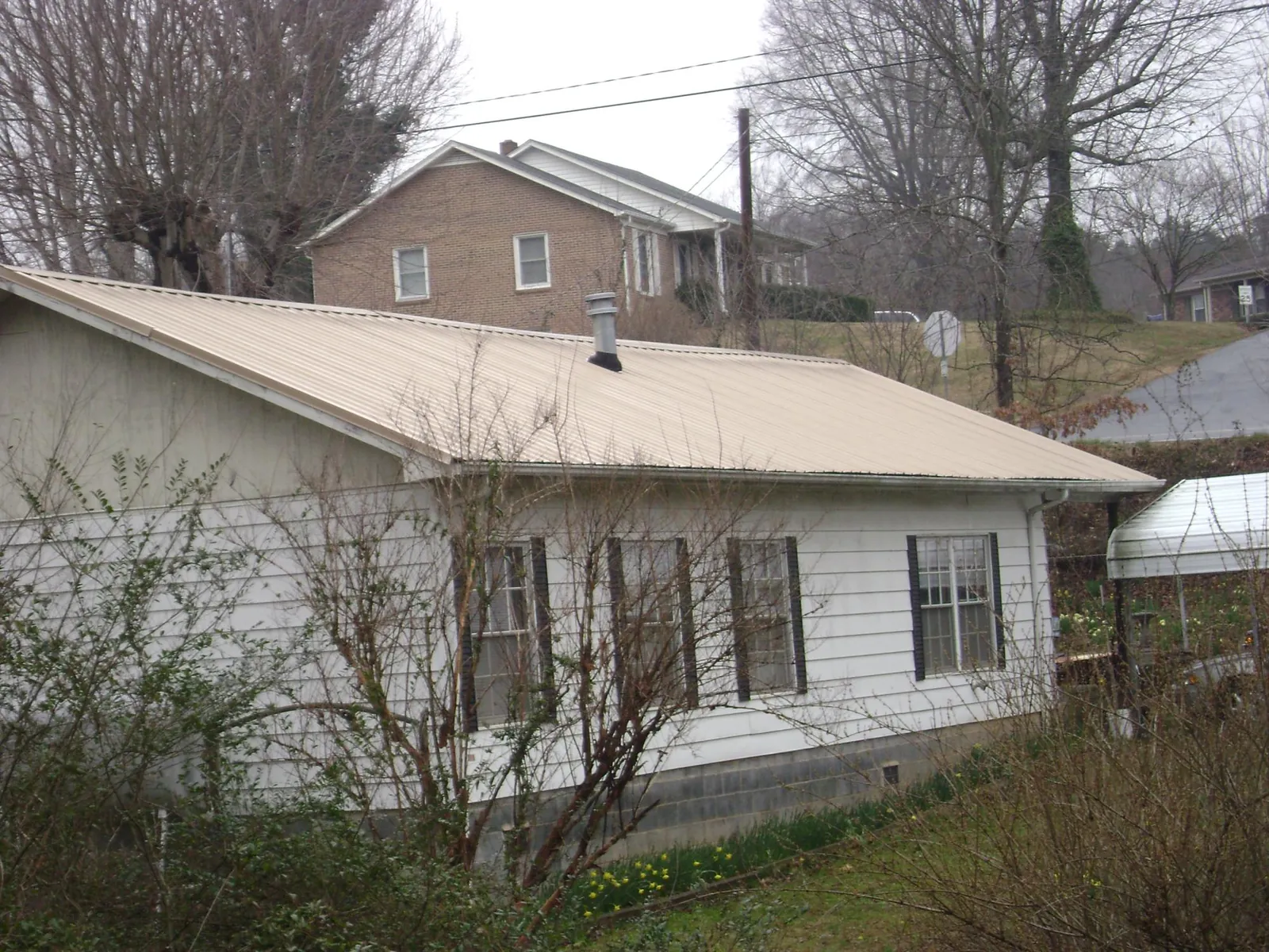 Tan metal roof on a white sided house set into a hillside — Commercial Roofing by Roofing Brothers in Fairdale